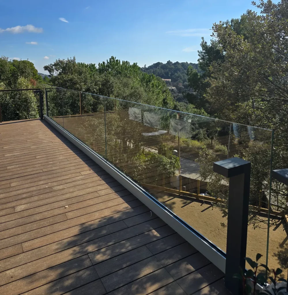Barandilla de vidrio transparente en terraza elevada con vistas a zona arbolada